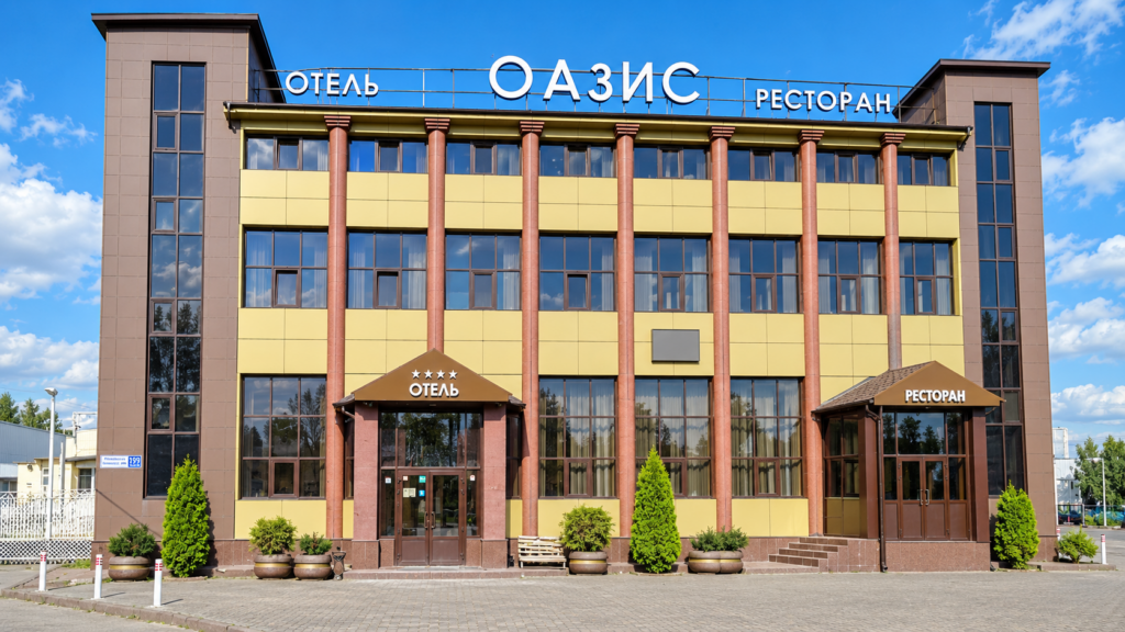 Фасад комплекса «Оазис» днём: вывески «Отель», «Оазис» и «Ресторан», входы в гостиницу и ресторан